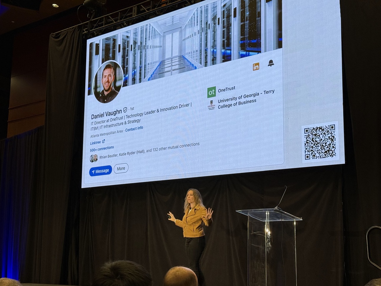 Kelly speaking on stage with a photo of her husband's LinkedIn profile on screen